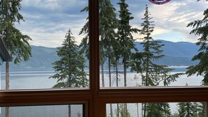 A view from a window overlooking a lake with trees and mountains in the distance.