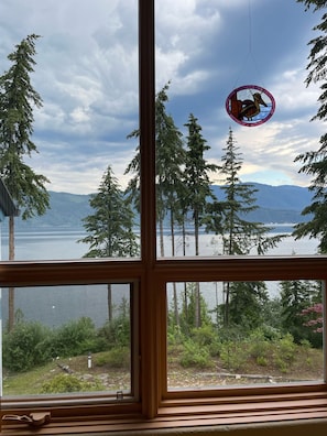 A view from a window overlooking a lake with trees and mountains in the distance.