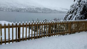 A wooden fence with snow accumulation, a snow-covered landscape, and a body of water in the background.