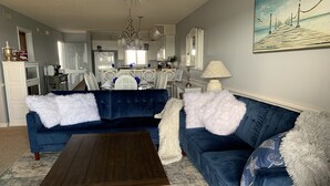 A living room with a dark blue sofa, white fluffy pillows, a wooden coffee table, and a patterned rug.