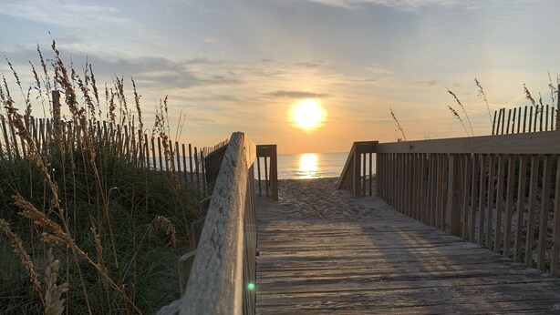 A wooden boardwalk leading to the beach with a sunset in the background.