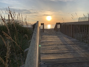 A wooden boardwalk leading to the beach with a sunset in the background.