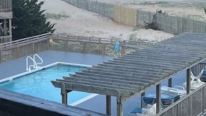 A pool with a wooden deck, a beach view, and a wooden fence.
