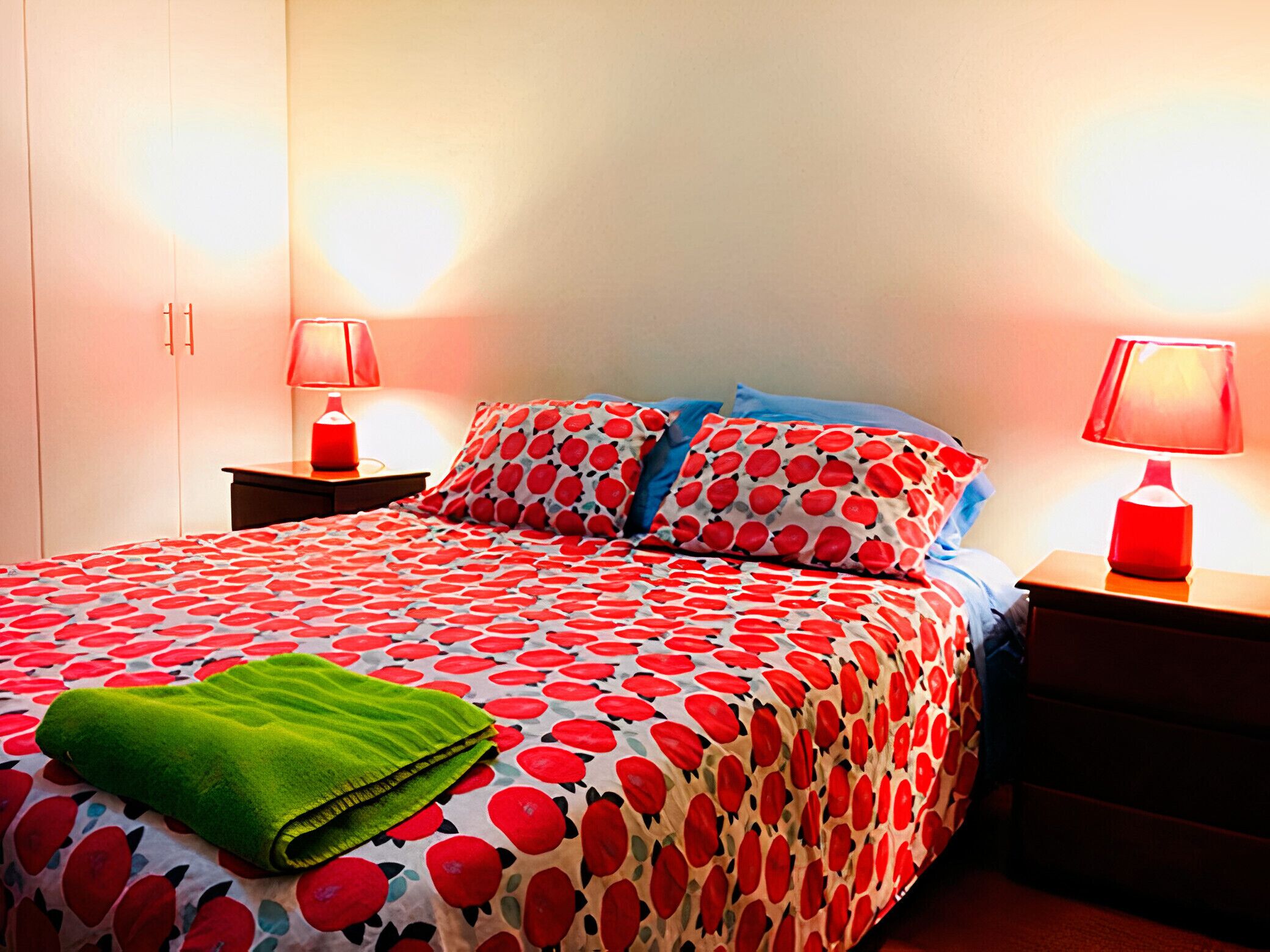 A neatly made bed with a patterned bedspread, two bedside lamps, and a green towel on the bed.