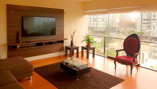 A modern living room with a flat-screen TV, comfortable seating, a small coffee table, and a balcony with a view of the city. - Nice Apartment Malecon Balta Miraflores (Lima)