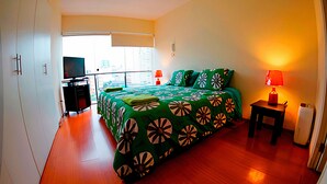 A hotel room with a large bed, a TV, a desk, and a balcony with a city view. - Nice Apartment Malecon Balta Miraflores (Lima)