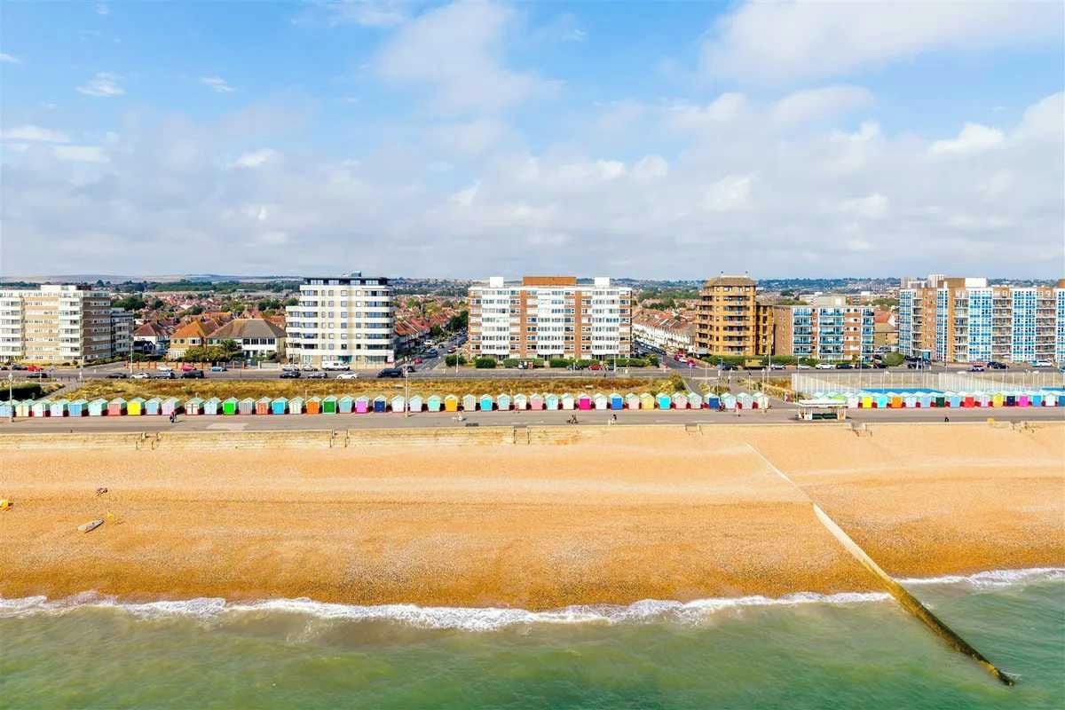 A coastal cityscape with a beach, colorful beach huts, and high-rise residential buildings.