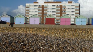 A row of colorful beach huts with a stone wall in the foreground and a multi-story building in the background. - With spectacular sea views the flat is literally across the road from the Beach. (Hove)