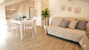 Une pièce moderne et bien éclairée, comprenant un coin repas, un canapé et une grande plante.