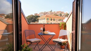 Un balcon avec deux chaises, une petite table et une bouteille, donnant sur un paysage urbain avec des bâtiments.