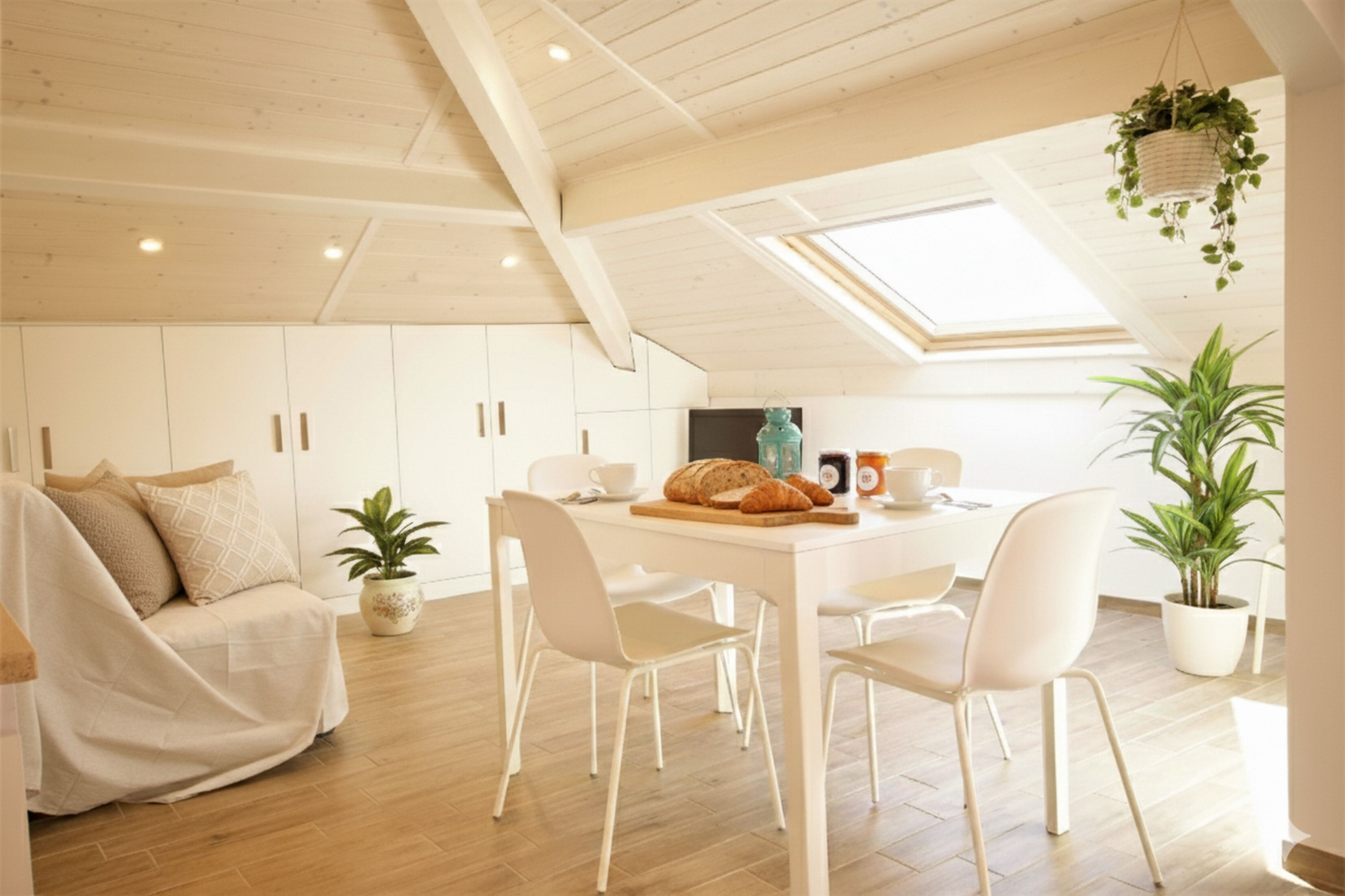 A modern kitchen with white cabinetry, a dining table, chairs, and a skylight.