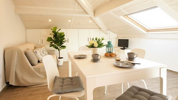 Une pièce confortable de style loft, comprenant un coin repas, un canapé recouvert d’un tissu douillet et une grande fenêtre laissant entrer la lumière naturelle.
