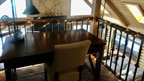 A wooden dining table with a chair, a stone wall, and a balcony railing with string lights. - Stunning Views from 3 Level Home, Majestic Sunrise and Mountain Scapes (Pine)