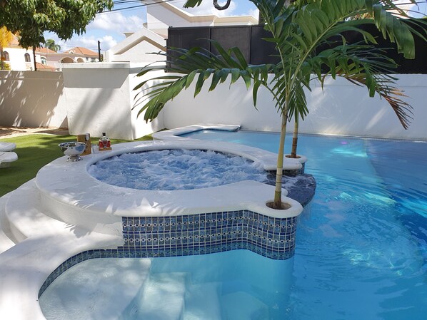 Relax by the pool surrounded by a lush lawn and a palm tree.
