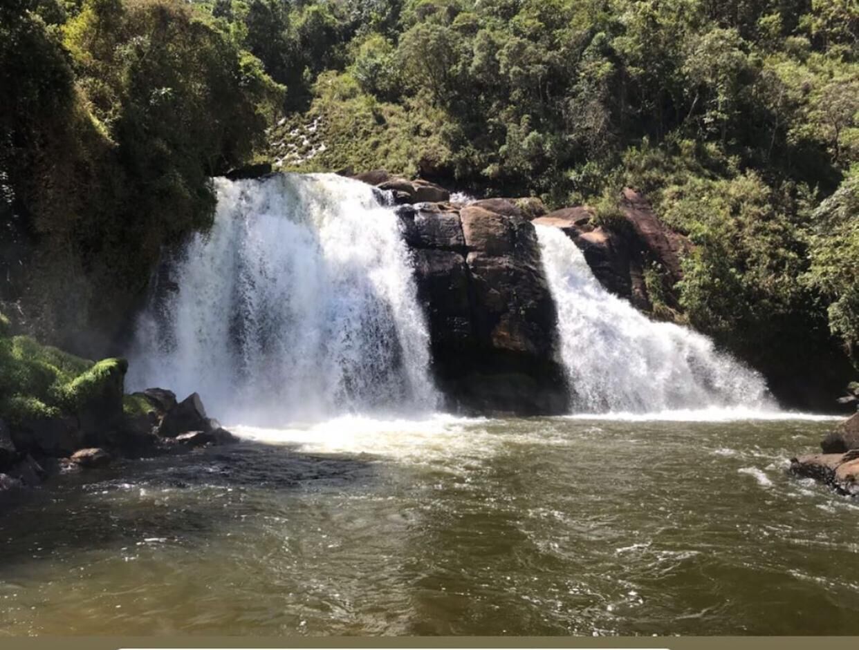 Ein Wasserfall stürzt über Felsen in einen Fluss, umgeben von dichtem Grün.