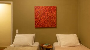 A hotel room with two beds, a small wooden table, and a colorful abstract painting on the wall. - Duplex apartment in a guesthouse in the Bocaina mountains with a view of the lake. (Bananal)