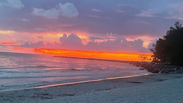 A beach with a sunset, waves, and a pier.