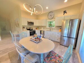 A modern kitchen with white cabinets, a stainless steel refrigerator, a microwave, and a dining area with a white table and chairs.