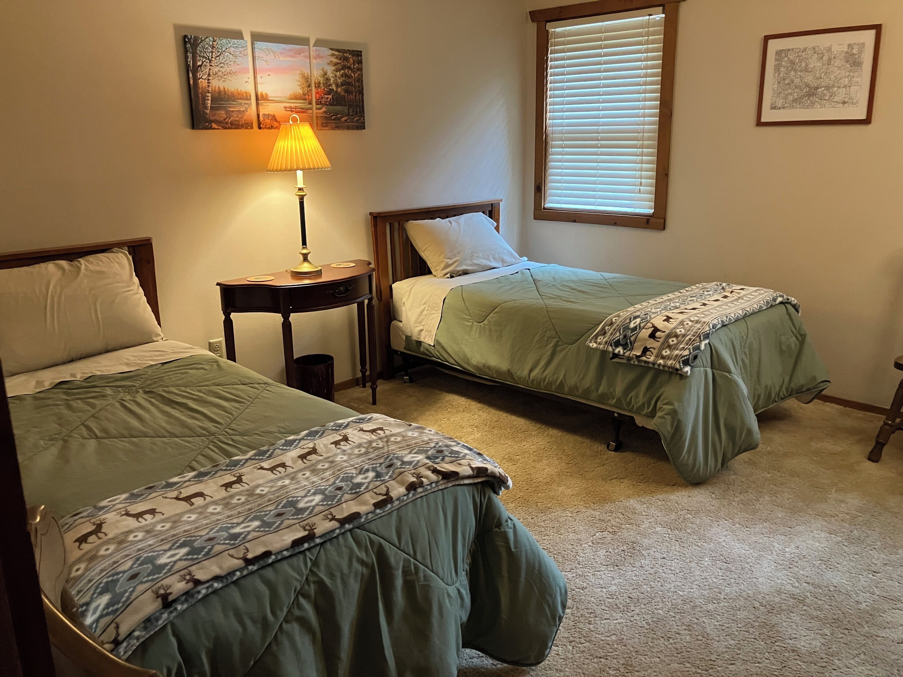 A bedroom with two single beds, a bedside table with a lamp, and a window with blinds.