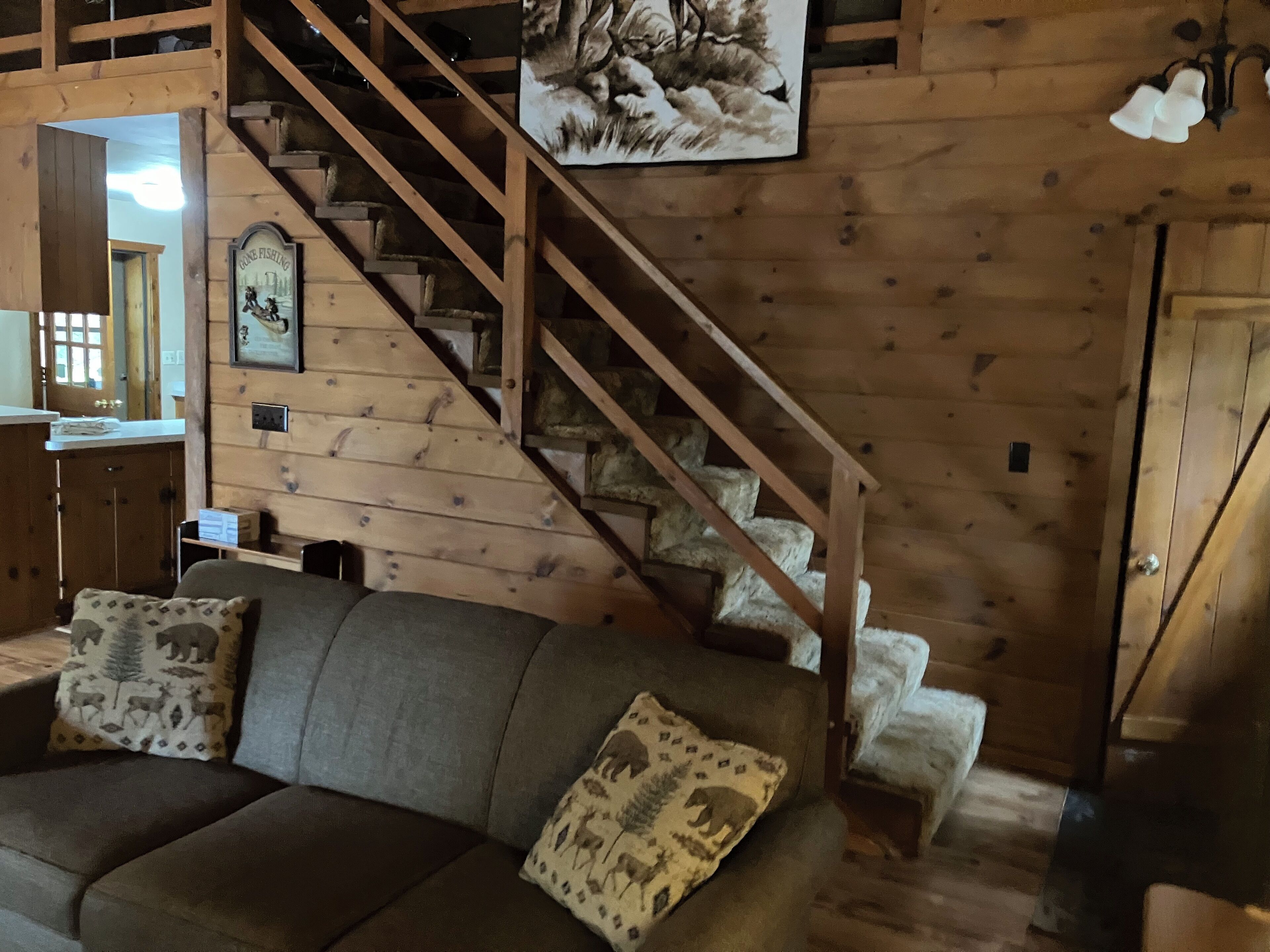 Un intérieur en bois avec un escalier, un canapé agrémenté de coussins à motifs et un tableau encadré au mur.