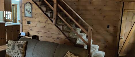 Un intérieur en bois avec un escalier, un canapé agrémenté de coussins à motifs et un tableau encadré au mur.