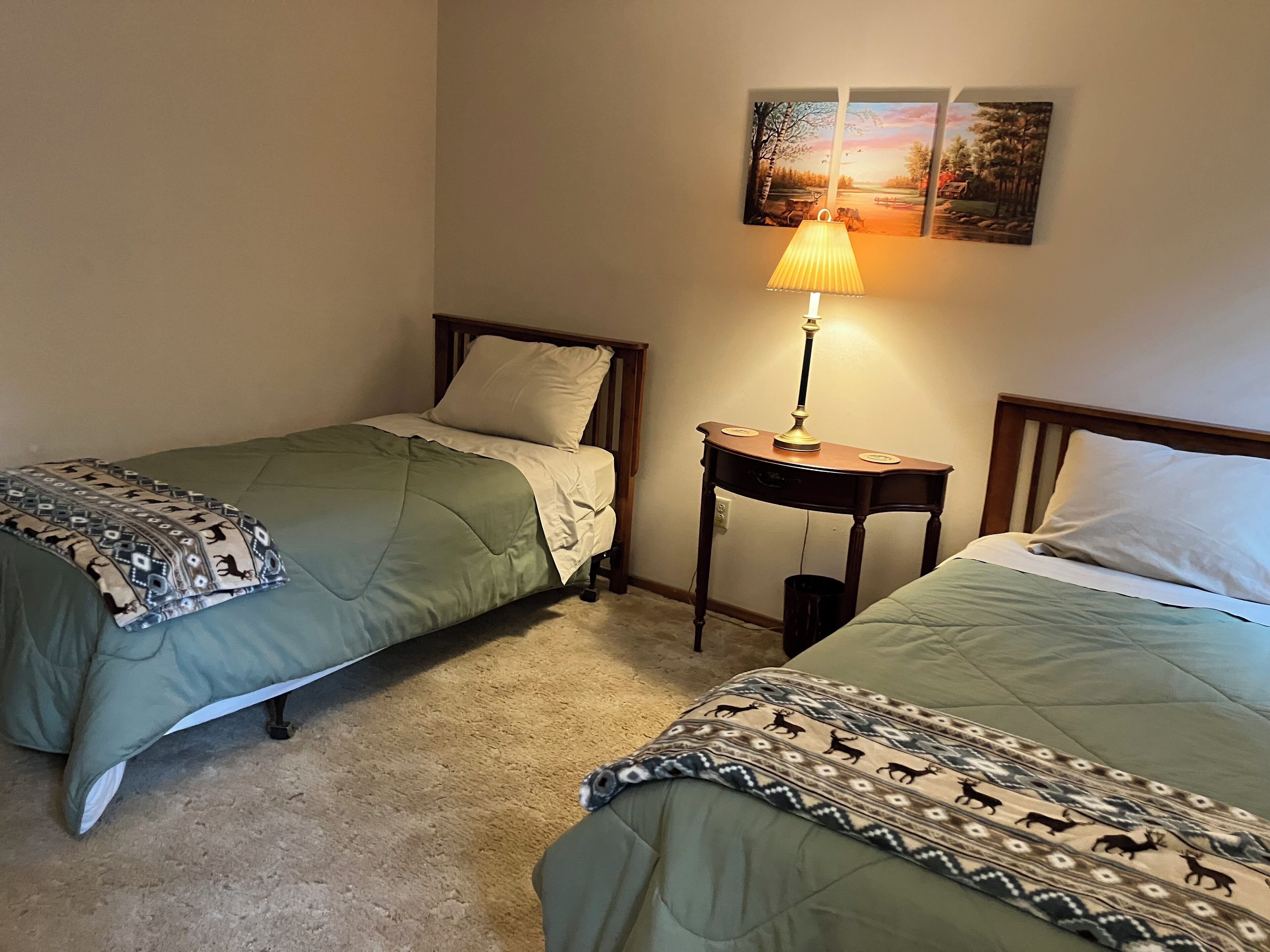 A bedroom with two single beds, a bedside table with a lamp, and a wall-mounted painting.