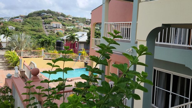 A multi-story building with a swimming pool, surrounded by greenery and a hilly landscape in the background.