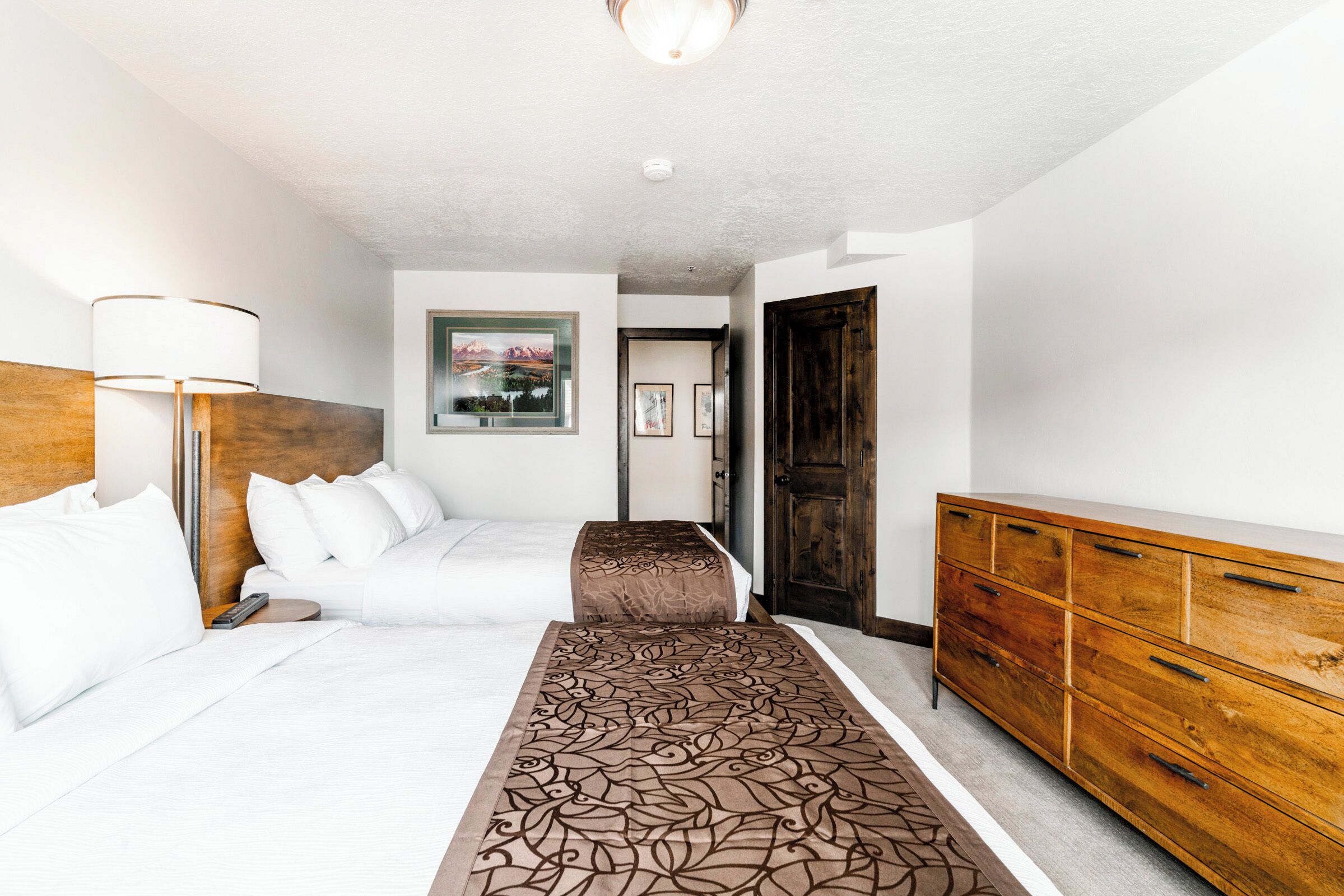 Une chambre d’hôtel avec un lit, une table de chevet, une lampe, une commode et un tableau au mur.