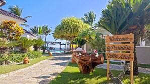 A wooden sign welcoming to Paradise Villa Azul, a resort with a pool, lounge chairs, and tropical landscaping.
