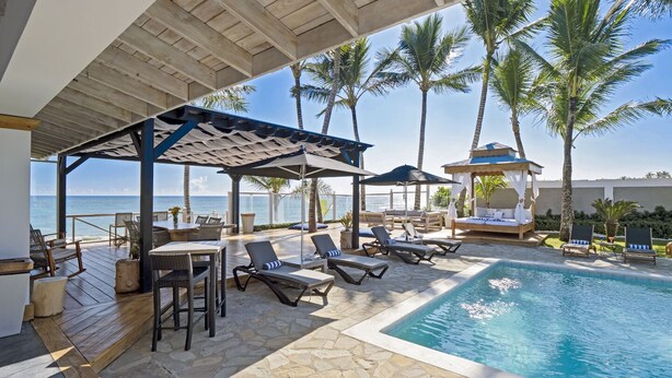 A poolside area with lounge chairs, a covered seating area, and a view of the ocean.