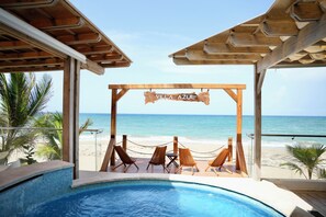 A wooden deck with lounge chairs overlooking a beach and pool.