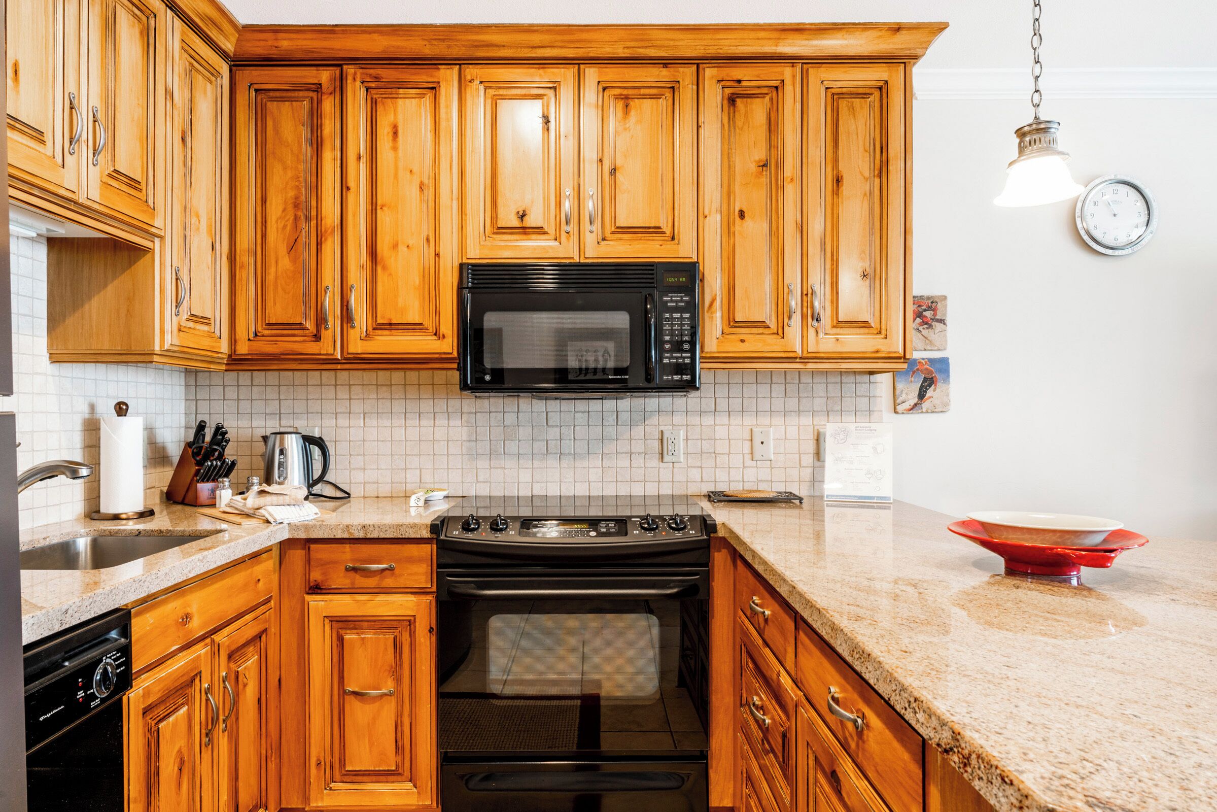 A kitchen with wooden cabinets, a black microwave, a stove, and a sink.