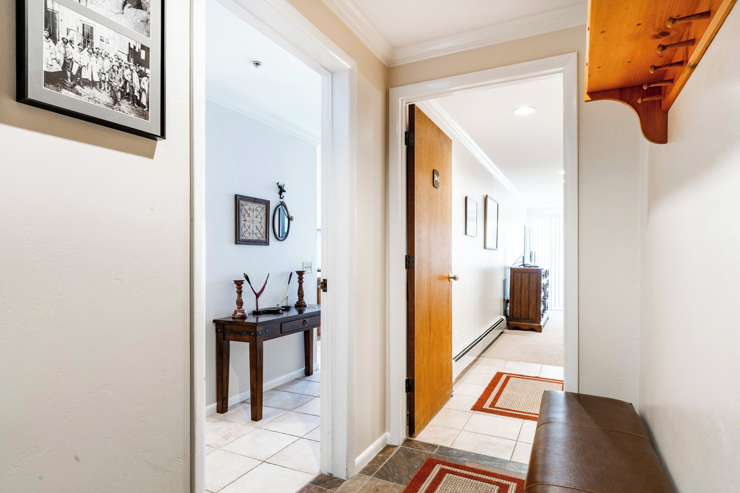 Un pasillo con un banco de madera, una fotografía enmarcada y una puerta que da a otra habitación.