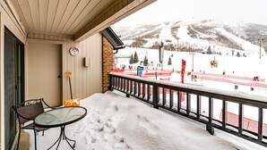 Ein Balkon mit Tisch und Stühlen, der Blick auf einen verschneiten Skipisten und einen Berg im Hintergrund bietet.