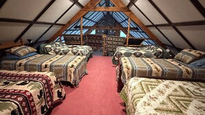 A cozy attic bedroom with four beds arranged in a U-shape, a red carpet, and a stone wall.
