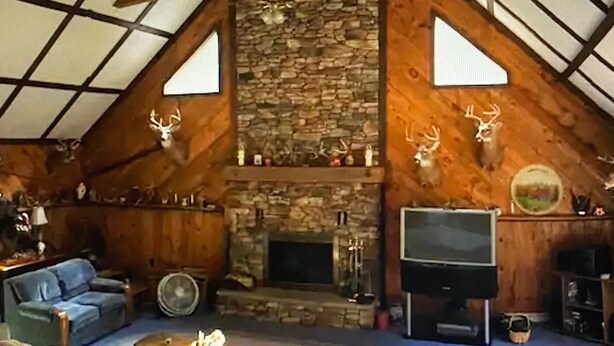 A rustic living room with a stone fireplace, wooden beams, and deer antlers decor.