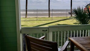 A balcony with a view of the beach, palm trees, and a fence. - Mermaid Landing Beachfront Condo with WIFI, Pools, and Hot Tub (Galveston)