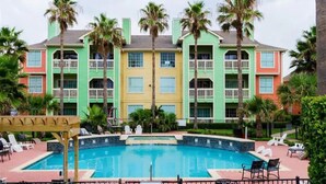 A multi-story hotel with a swimming pool surrounded by palm trees and lounge chairs. - Mermaid Landing Beachfront Condo with WIFI, Pools, and Hot Tub (Galveston)