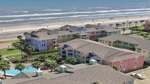 A beachfront hotel with colorful buildings, a swimming pool, and a beach view. - Mermaid Landing Beachfront Condo with WIFI, Pools, and Hot Tub (Galveston)