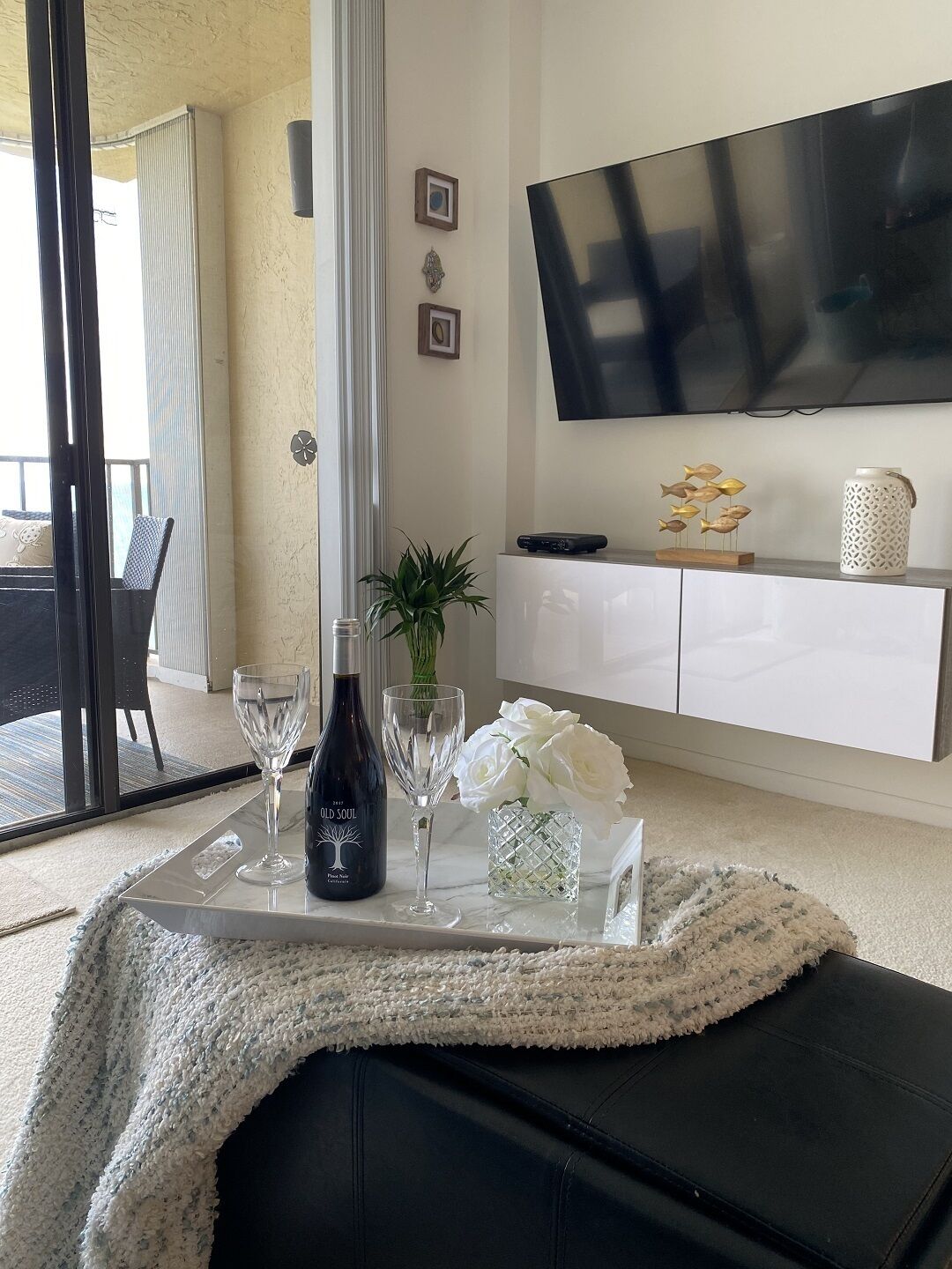Een moderne woonkamer met een glazen salontafel, een fles wijn en decoratieve objecten.