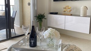 Un soggiorno moderno con un tavolino da caffè in vetro, una bottiglia di vino e oggetti decorativi.