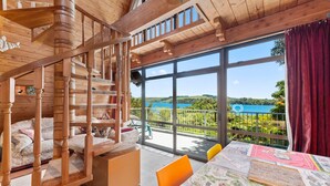A wooden interior with a spiral staircase, a dining area with a table covered in a map, and a balcony with a view of a lake and greenery.
