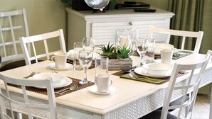 A dining table set with white plates, cups, and cutlery, surrounded by white chairs.