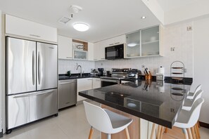 Una cocina moderna con electrodomésticos de acero inoxidable, una isla central con asientos y armarios blancos.