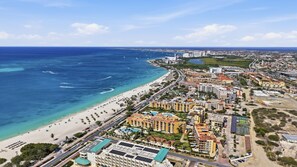 Un paisaje urbano costero con un hotel frente a la playa, cielos despejados y vista al océano.