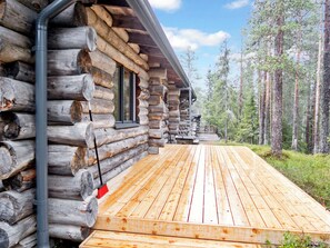 A log cabin with a wooden deck and a metal pipe on the exterior wall.