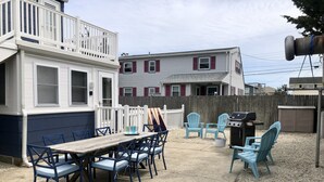 A backyard with a wooden table and blue chairs, a barbecue grill, and a white fence. - Newly renovated Cape Cod 4BR 2 Baths in LBI close to restaurants, and beach (Ship Bottom)
