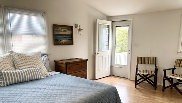 A bedroom with a bed, a dresser, a chair, and a door leading outside. - Newly renovated Cape Cod 4BR 2 Baths in LBI close to restaurants, and beach (Ship Bottom)