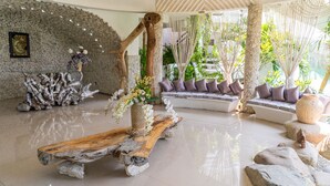 A spacious lobby with a stone wall, a wooden bench with a vase of flowers, and a seating area with cushions.