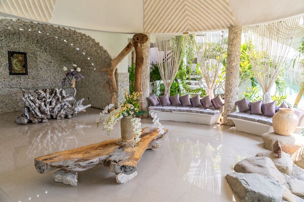 Un vestíbulo amplio con una pared de piedra, un banco de madera con un florero y una zona de estar con cojines.